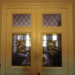 Rechthoekige glasramen gevat in 2 deuren met in het midden een afbeelding van Flor Coucke