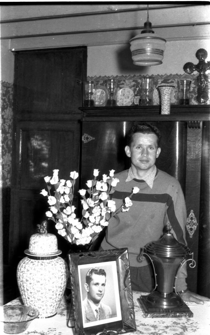 Wielrenner Pol Rosseel poseert in kamer bij foto, beker en bloemen, Izegem 1957