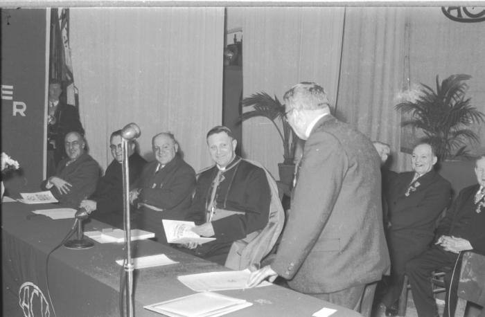 Lachende Mgr. Desmedt houdt een boek in de hand, Izegem 1957