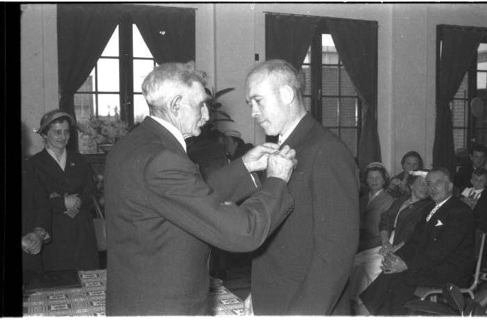 Huldiging gedecoreerden Unions: burgemeester speldt het ereteken op bij een mijnheer, Izegem 1957