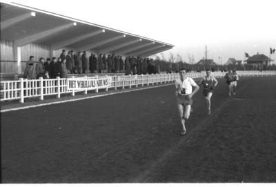 Fotoreportage atletiekwedstrijd: Vanderhoeven loopt voorbij tribune, Izegem 1957